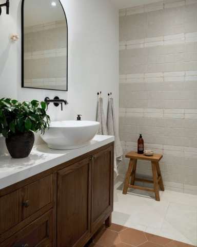 Bathroom with a walnut vanity, arched mirror and textured tile wall, from a Shan Carlsson Interiors project