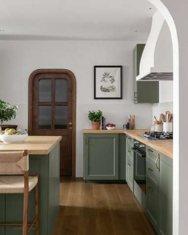 Sage green kitchen cabinetry with natural wood countertop and an arched doorway, from a Shan Carlsson Interiors residential project